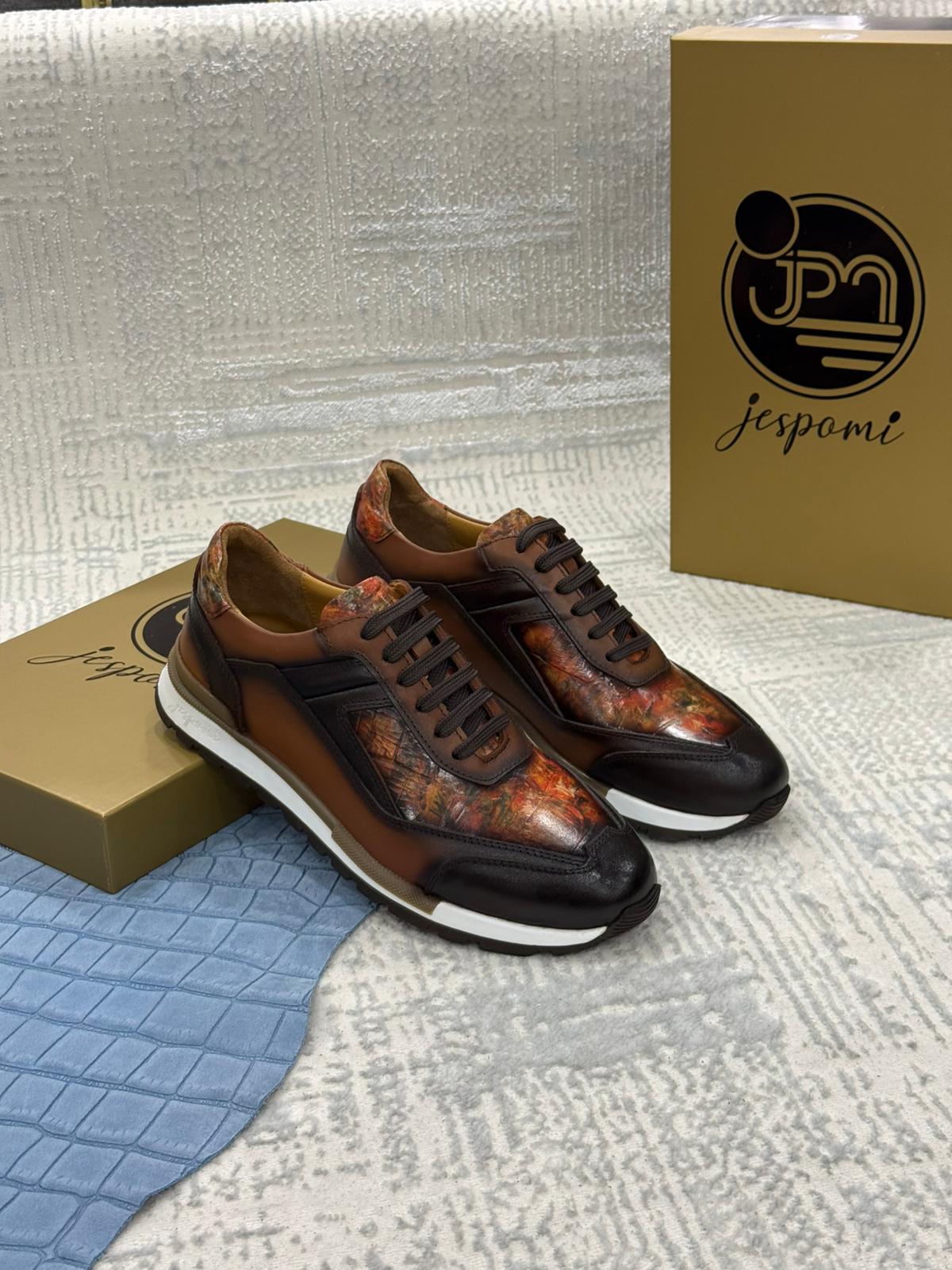Sneakers homme en cuir marron patiné avec empiècements artistiques aux nuances cuivrées et semelle sportive blanche, présentées dans un écrin de marque Jespomi
